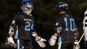 Two lacrosse players exchange a high five on a lacrosse field at night