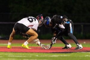 Two opposing lacrosse players face off on center field